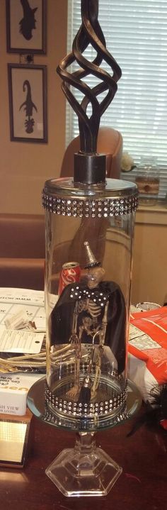 a glass vase with a skeleton inside sitting on a table next to books and papers