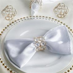 a white plate topped with a silver bow tie next to gold beaded napkins