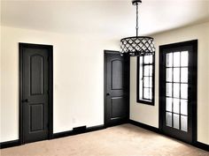 an empty room with two black doors and a chandelier