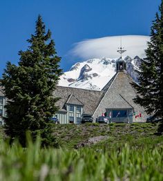 the building is surrounded by trees and snow capped mountain in the background with clouds above it