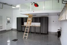 a ladder is hanging from the ceiling in an empty room with black cabinets and white walls