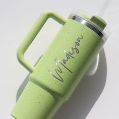 a green cup with the word macaroni written on it sitting next to a white background