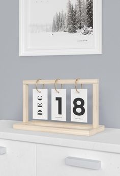 a white dresser with two calendars on it and a black and white photo hanging above the drawers