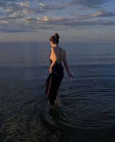 a woman wading in the ocean with her back turned to the camera and wearing a black dress