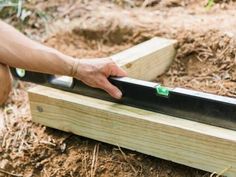 a person holding a knife over a piece of wood in the ground with dirt and grass around it