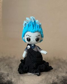 a crocheted doll with blue hair sitting on top of a table next to a wall