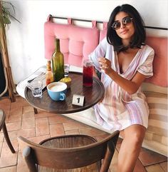 a woman sitting at a table with drinks and food on it, posing for the camera