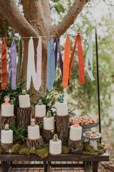 a table topped with cakes and desserts next to a tree trunk covered in moss