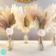 three vases with flowers and feathers in them on a white countertop next to a clock