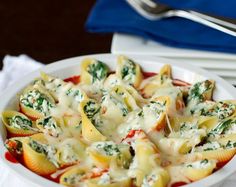 a white bowl filled with shells covered in cheese and spinach on top of a table