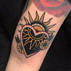 a heart tattoo with flowers and sun on the inside of it's side arm