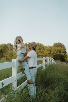 a man standing next to a woman on top of a white fence in tall grass