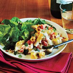 a white plate filled with pasta and spinach next to a glass of water on a wooden table