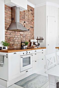 a kitchen with brick walls and white cabinets is pictured in this image, there are chairs around the table