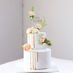 a three tiered cake with flowers and greenery on the top is decorated with a happy birthday sign