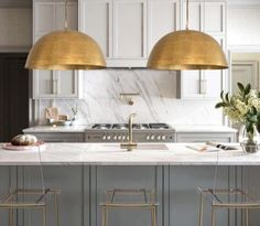 two gold pendant lights hanging over an island in a kitchen with marble counter tops and stools