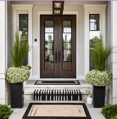 two planters with plants are on the front step of a house that is decorated in black and white