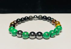 Hand-made bracelet, combining artwork with natural healing gemstones. This design represents the a lush mountain above a rich foundation, with hematite peaks. Stones used in this bracelet: - Hematite, green malachite, black obsidian, black lava, yellow tiger eye, red tiger eye, brown bronzite, black lava. - Aids with positivity, calm, balance, stress relief, self-esteem, and self-expression Each bracelet is hand-made upon ordering. Each size varies with stone usage while following the basic pattern of the artwork. SIZE: Please measure where you will wear the bracelet. A soft seamstress-style measuring tape can be used to provide the measurement of the wrist. PRODUCTION & SHIPPING: - All items are made to order - Your order will be created and shipped within 2-4 business days - Shipping tim Spiritual Hematite Beaded Bracelet With Natural Stones, Healing Hematite Bracelets With Natural Stones, Healing Hematite Bracelet With Natural Stones, Hematite Beaded Bracelets With Natural Stones As Gift, Handmade Hematite Crystal Bracelet Gift, Spiritual Hematite Bracelet With Natural Stones, Hematite Stretch Bracelet As Gift, Handmade Hematite Spiritual Bracelets, Hematite Bracelets With Natural Stones For Gift