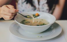 a woman is eating soup from a bowl on a plate with a spoon in her hand