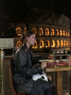 a woman sitting at a table eating food in front of the colossion, rome