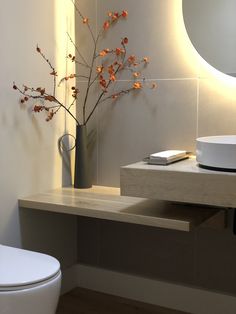 a white toilet sitting next to a sink in a bathroom under a large round mirror