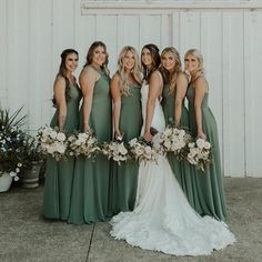 a group of women standing next to each other in front of a white wall holding bouquets