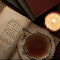 an open book next to a lit candle and teacup on a plate with saucer