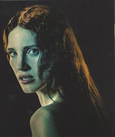 a woman with long hair and blue eyes stares into the distance while standing in front of a black background