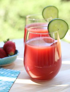 two glasses filled with tomato and cucumber garnish on top of a wooden table