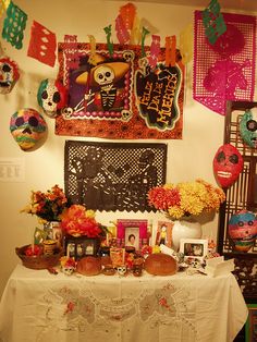 a table topped with lots of decorations and flowers next to a wall covered in mexican masks