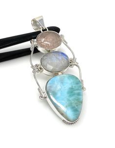 Larimar with Blue Flash Moonstone and Morganite Gemstone Sterling Silver Pendant Jewelry at Wholesale Price. SIZE : 2.75” X 1.15” ( including Bail) ( LXW ) *Width mentioned is at its widest * WEIGHT : 16.2g GEMSTONE : NATURAL LARIMAR , RAINBOW MOONSTONE AND MORGANITE TREATMENT: NO TREATMENT METAL : 925 STERLING SILVER ORIGIN - LARIMAR : DOMINICAN REPUBLIC HANDMADE **All Measurements are close approximations** LARIMAR : Larimar is the embodiment of the tranquil Sea and Sky energies. Its soft, soothing blues and calming turquoise is streaked with white patterns that resemble sunlight dancing beneath Caribbean waters. It brings the ancient wisdom of Atlantis and the healing power of dolphins to harmonize the body and soul. Larimar has a vitreous to silky luster. Larimar is a stone of great wi Morganite Gemstone, San Ramon, Silver Jewelry Pendant, Pendant Silver, Wrapped Pendant, Wire Wrapped Pendant, Bohemian Jewelry, Morganite, Rainbow Moonstone