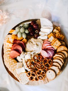 a platter with cheese, crackers, grapes and pretzels on it