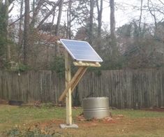 a small solar panel on top of a wooden pole in a yard next to a metal barrel