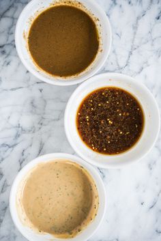 three bowls filled with marinades and sauce on top of a marble counter