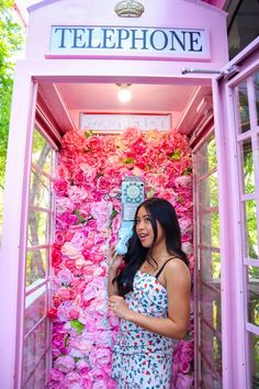 a woman standing in a phone booth with pink flowers on the wall and holding an umbrella