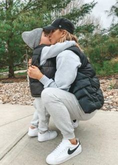 a woman kissing a man on the cheek while he is wearing a black jacket and grey sweatpants