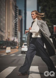 a woman is crossing the street with her coat over her shoulders