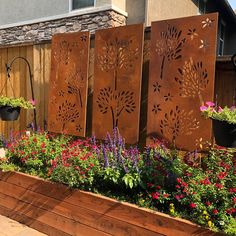 some flowers and plants are growing in a flower bed next to a fence that is made out of metal sheets