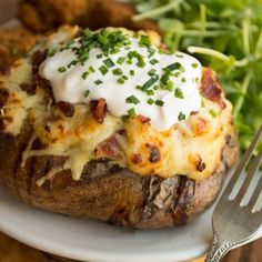 a white plate topped with baked potatoes covered in cheese and green onions next to a fork