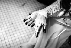 a woman with long black nails and white gloves on her arm, sitting in a tiled room