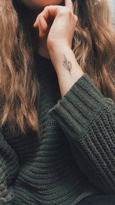 a woman with a feather tattoo on her wrist looking at the camera while holding her hand to her face