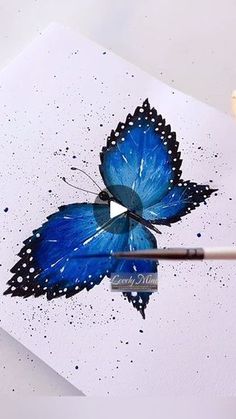 a blue butterfly is being drawn on a piece of paper with watercolor pencils