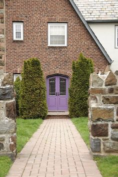 a purple door is in between two brick pillars on the side of a house that's surrounded by green grass and shrubbery