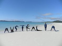 several people doing yoga on the beach with their arms in the air and one person standing behind them