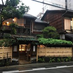 an old wooden building with green plants growing on it's roof line the street