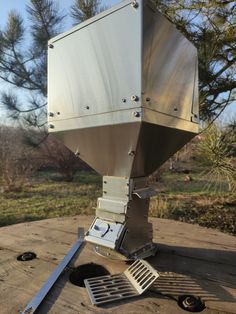 a large metal object sitting on top of a wooden table next to some trees and grass