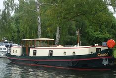 a boat that is sitting in the water next to some grass and trees on either side of it