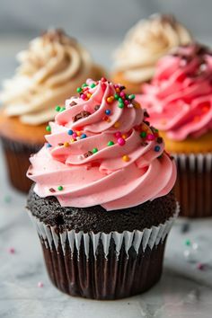 three cupcakes with pink frosting and sprinkles on the top