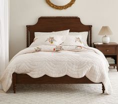 a bed with white sheets and pillows in a bedroom next to a nightstand, mirror and lamp