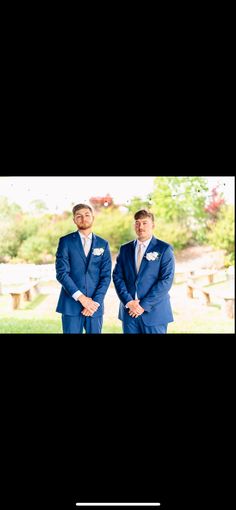 two men in blue suits standing next to each other with trees in the back ground